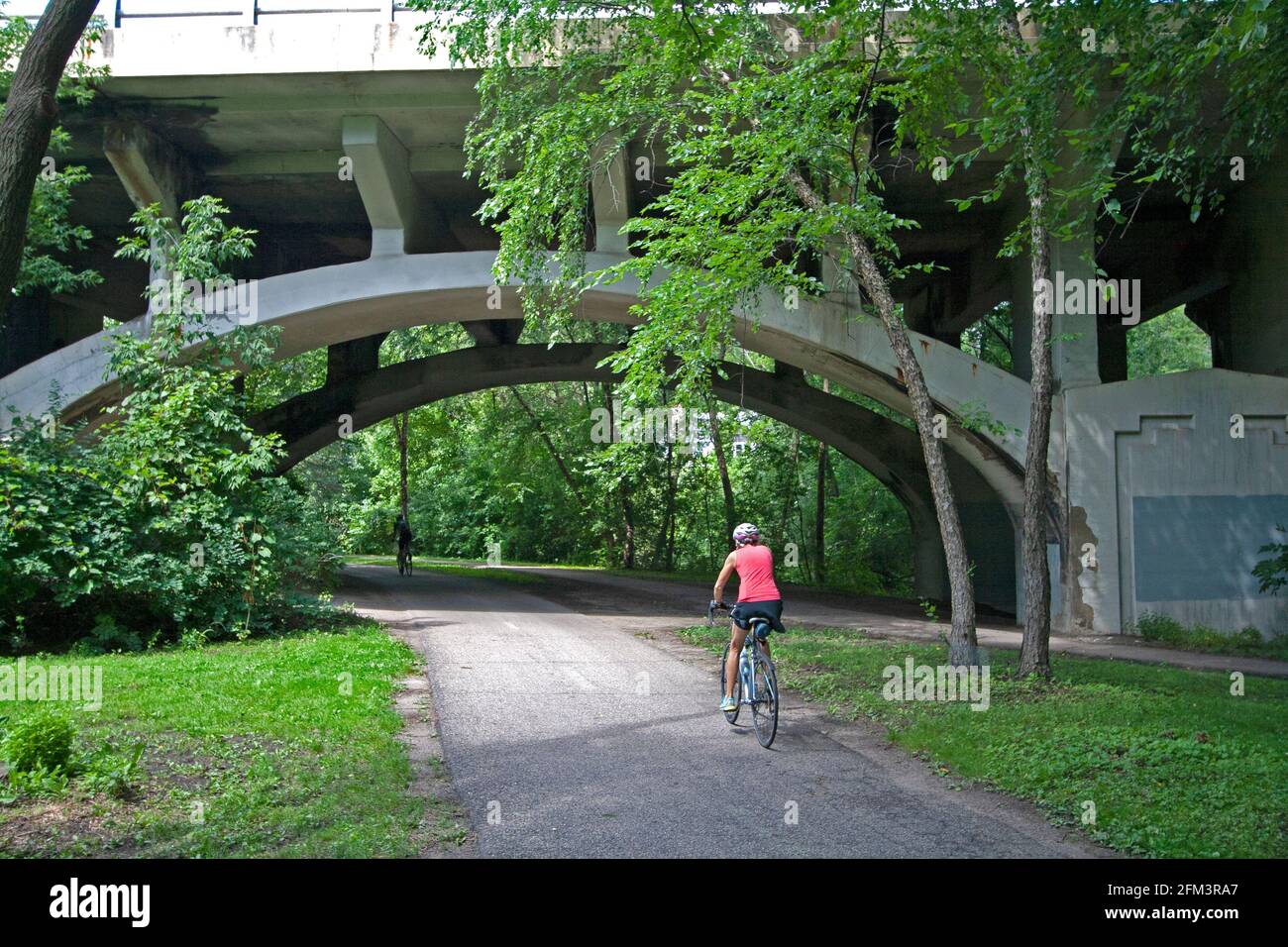 Bicycler peddling along the Minnehaha Parkway Regional Trail about to pass under the arch of the Nicollet Avenue Bridge. Minneapolis Minnesota MN USA Stock Photo
