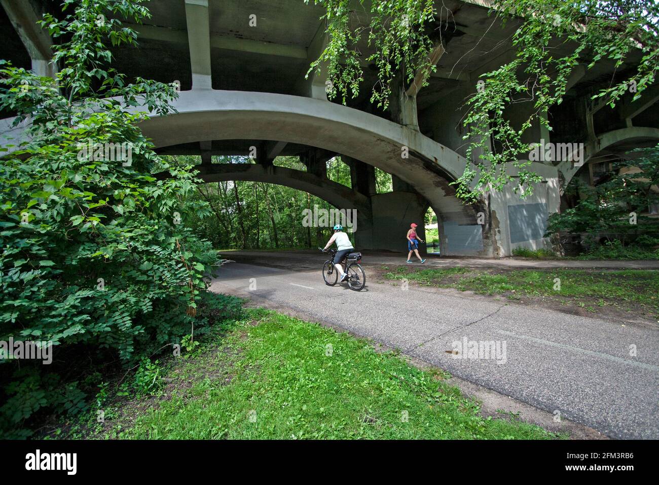Bicycler and walker pass under the arch of the the Nicollet Avenue Bridge along the Minnehaha Parkway Regional Trail. Minneapolis Minnesota MN USA Stock Photo