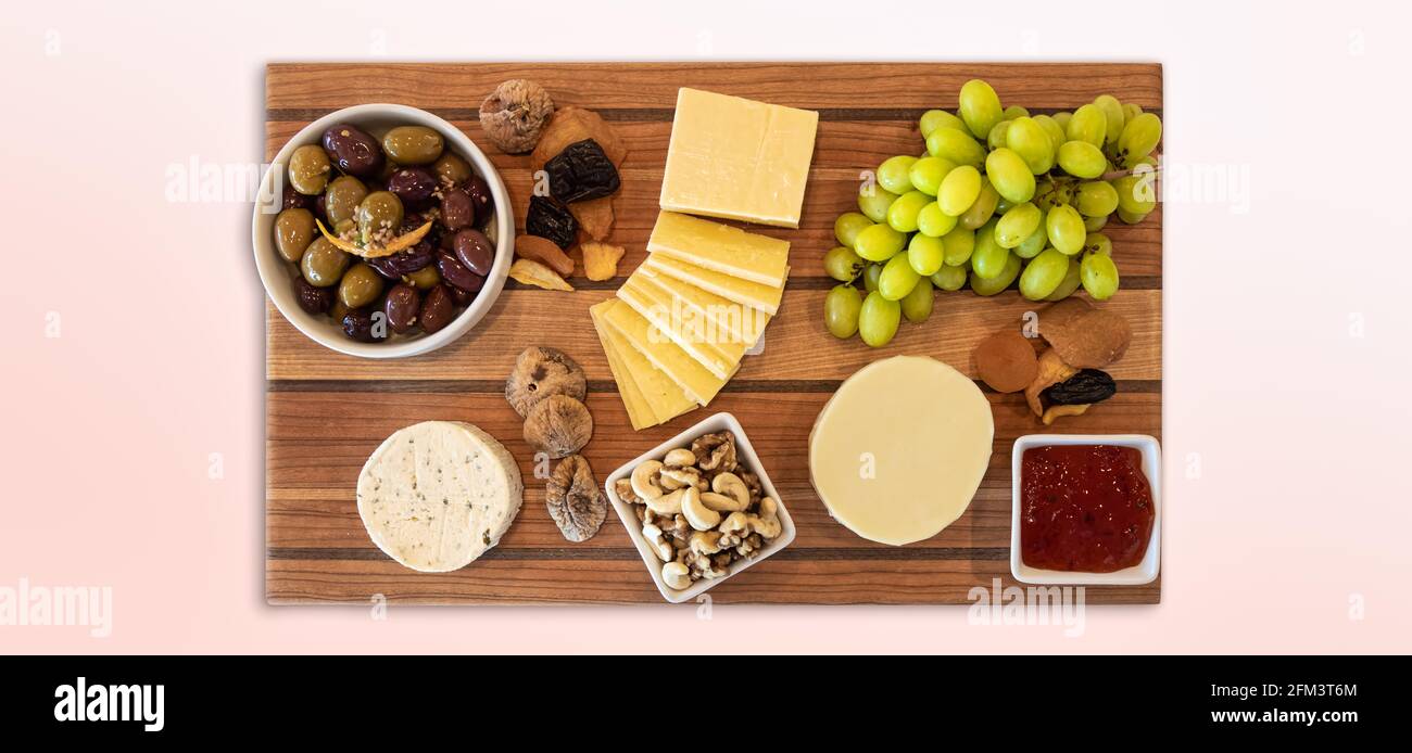 Cheese Assortment on a wooden board with fruit, nuts, jelly, and olives. Stock Photo