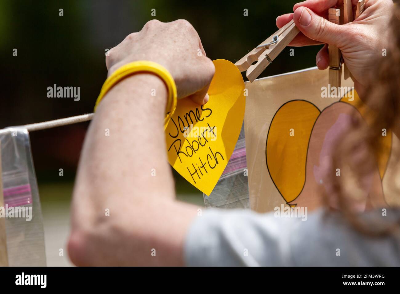 Washington, DC, USA, 5 May, 2021.  Pictured: A volunteer hangs yellow hearts on the Faces of Covid memorial during a rally to pressure the United States Government to waive patent protections for the Covid-19 vaccine and make it easily accessible to the rest of the world.  14 organizations joined to host the rally, recognizing that worldwide immunity is in everyone’s best interest.  Credit: Allison C Bailey / Alamy Live News Stock Photo