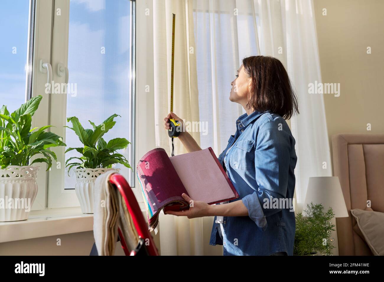 Female designer choosing curtain fabrics, measuring window with tape