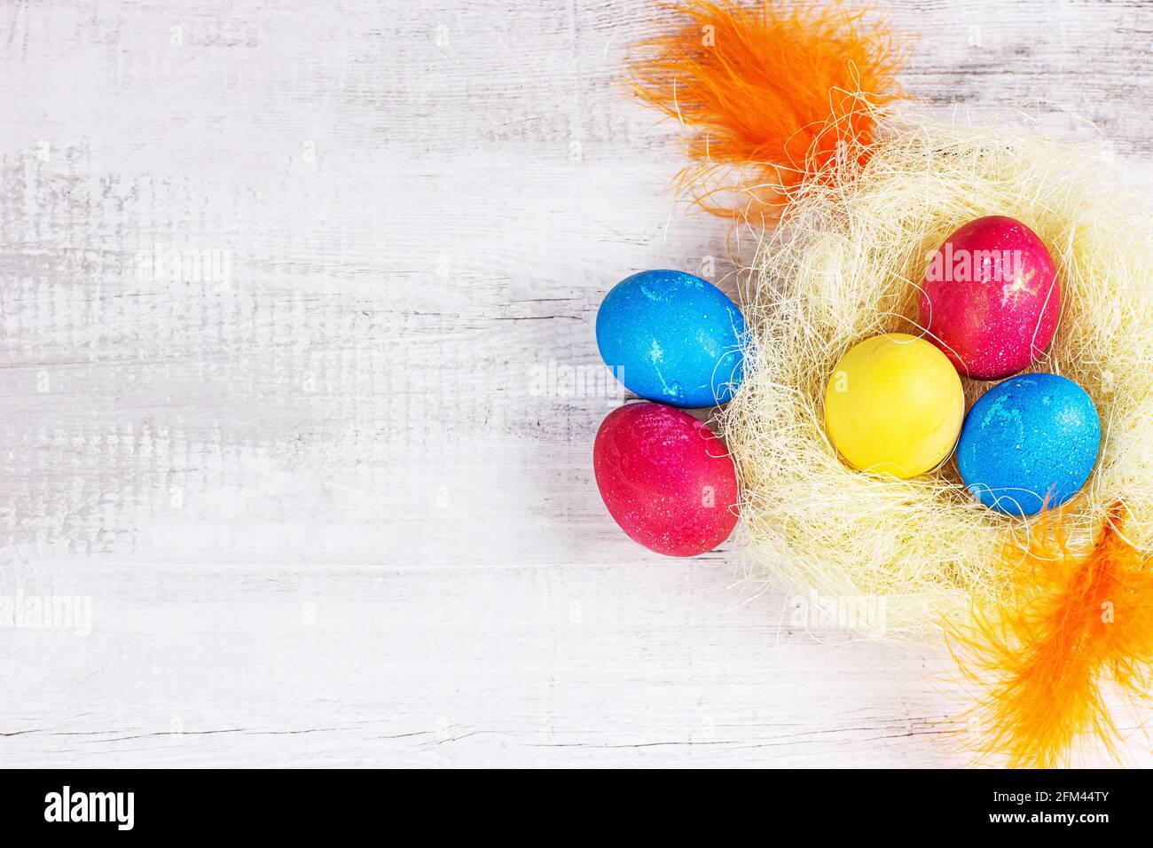 Top view flat lay colorful painted Easter eggs decorations in the nest with copy space on light wooden background. Stock Photo