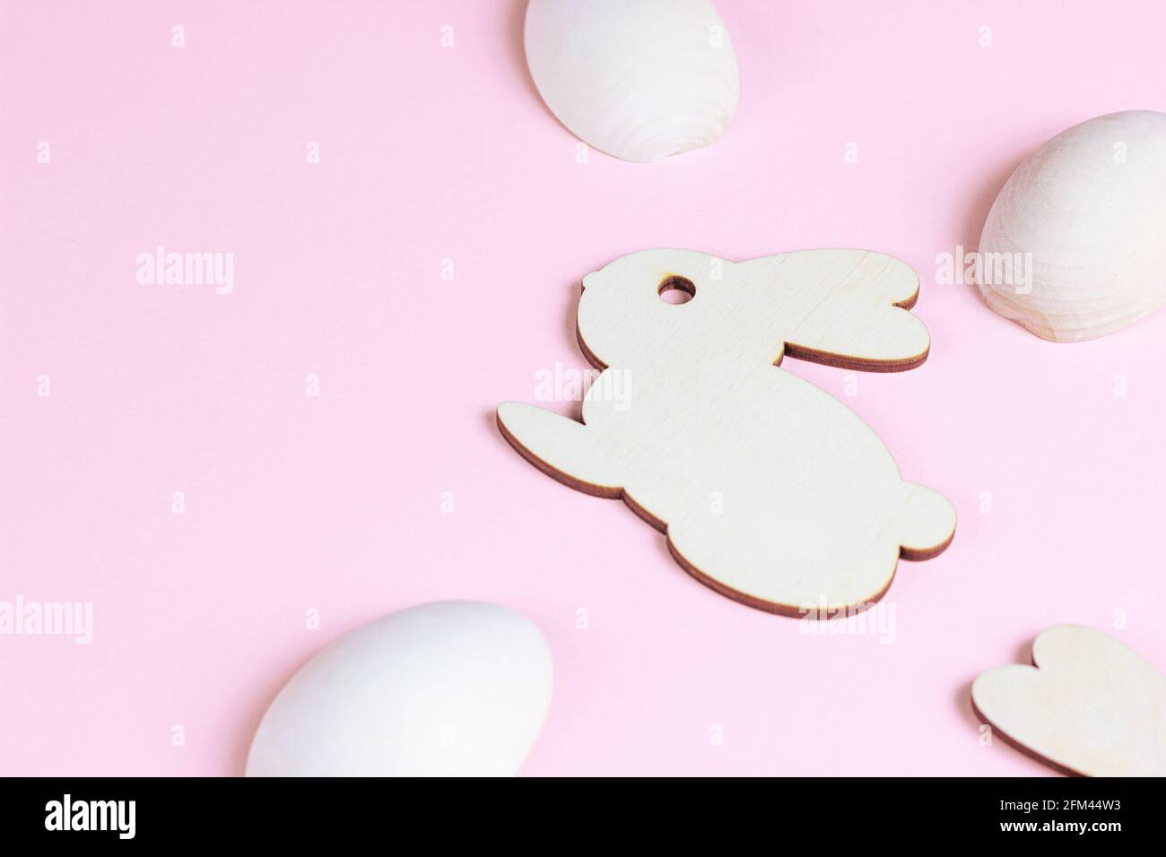 Funny wooden Easter Bunny with eggs as symbols of a holiday with copy space on light pink background. Stock Photo