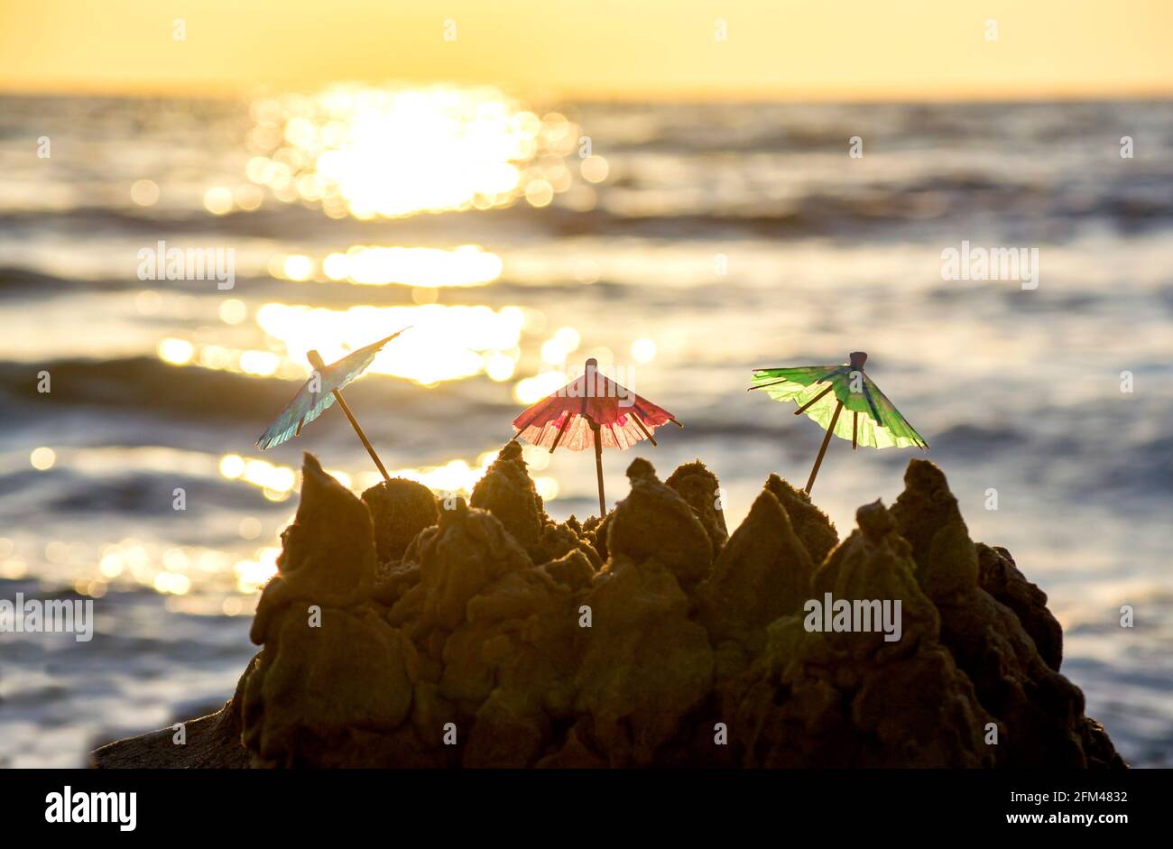 Small paper beach umbrellas stand for cocktail in sandy beach at sunrise. Stock Photo