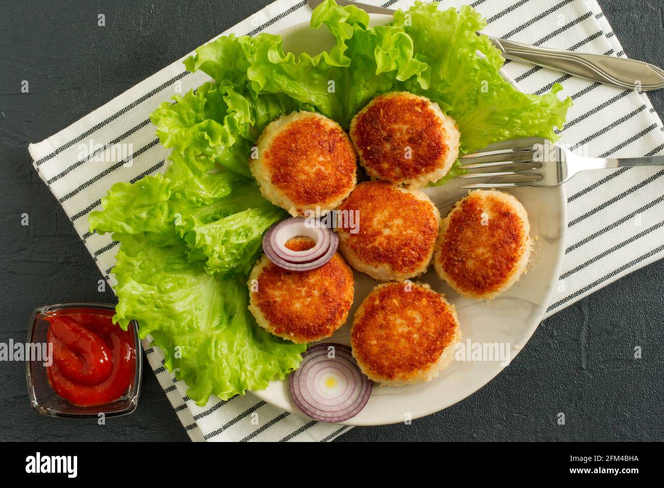 juicy delicious coated with breadcrumbs and fried chicken cutlets on white plate with spices and cetchup on dark background, view from above. Stock Photo