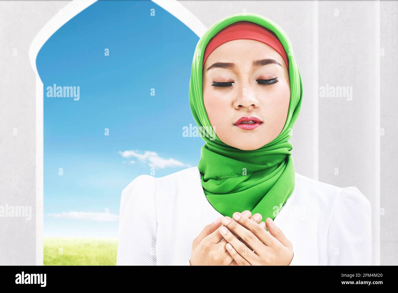 Asian Muslim woman in a veil sitting while raised hands and praying on ...