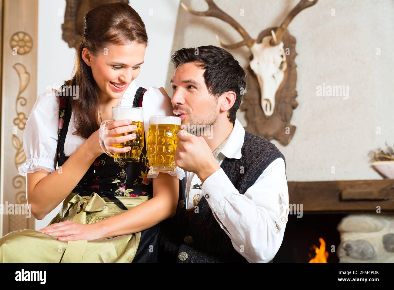 Couple in a traditional mountain hut with fireplace drinking beer Stock