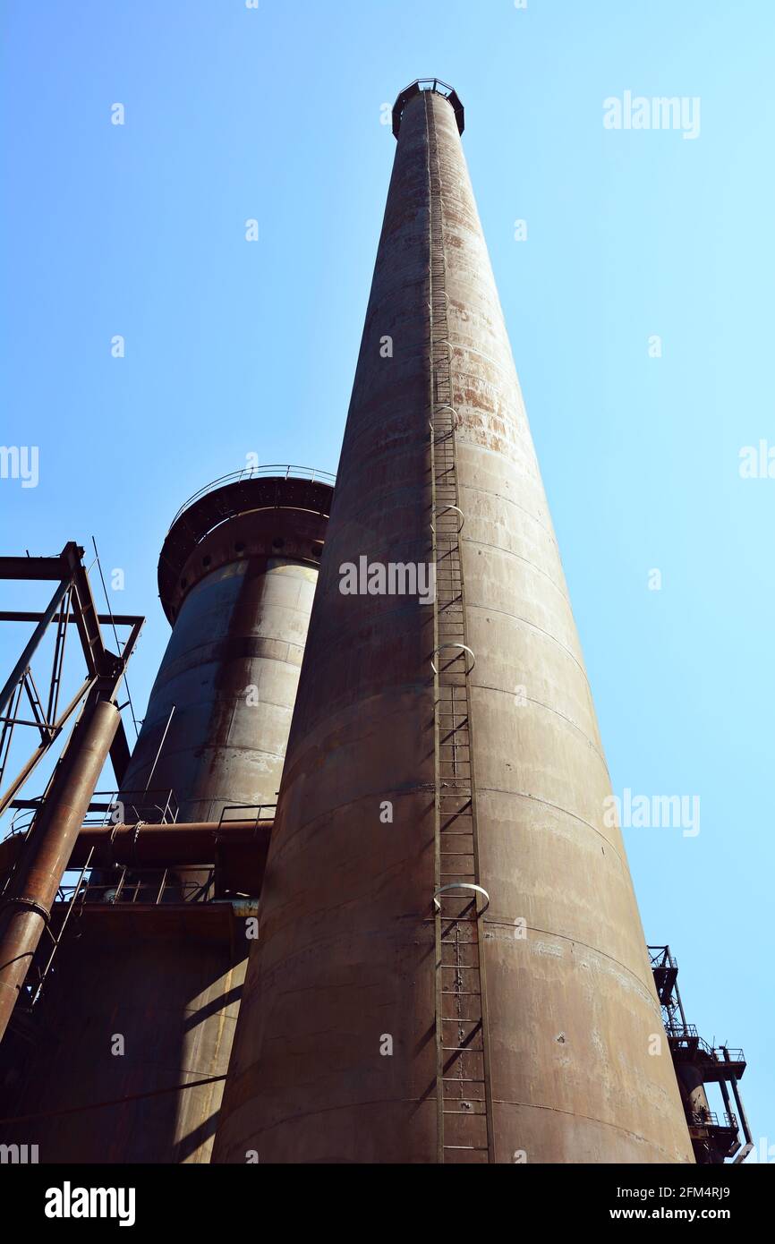 A bottom-up view of an old rusty chimney in front of blue sky at sunset light. Stock Photo
