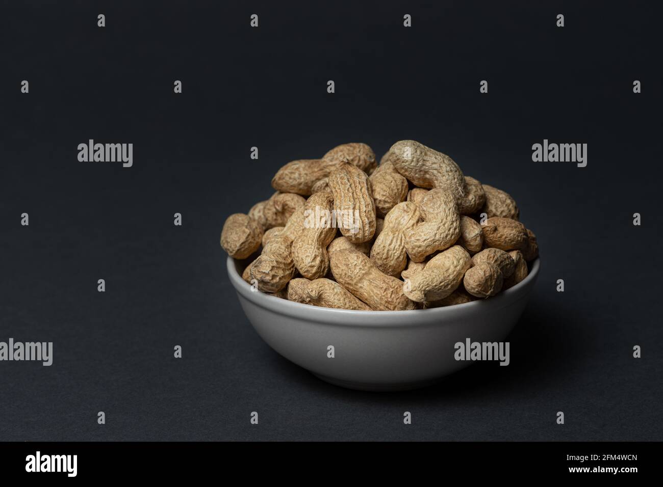 Unpeeled peanuts in bowl on dark background Stock Photo