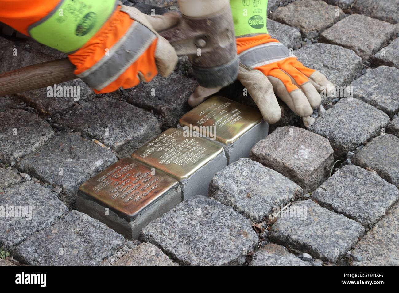 Chemnitz, Germany. 06th May, 2021. An employee of the municipal building  yard lays Stolpersteine on the pavement of Ludwig-Kirsch-Straße. A total of  27 new Stolpersteine are laid in memory of victims of