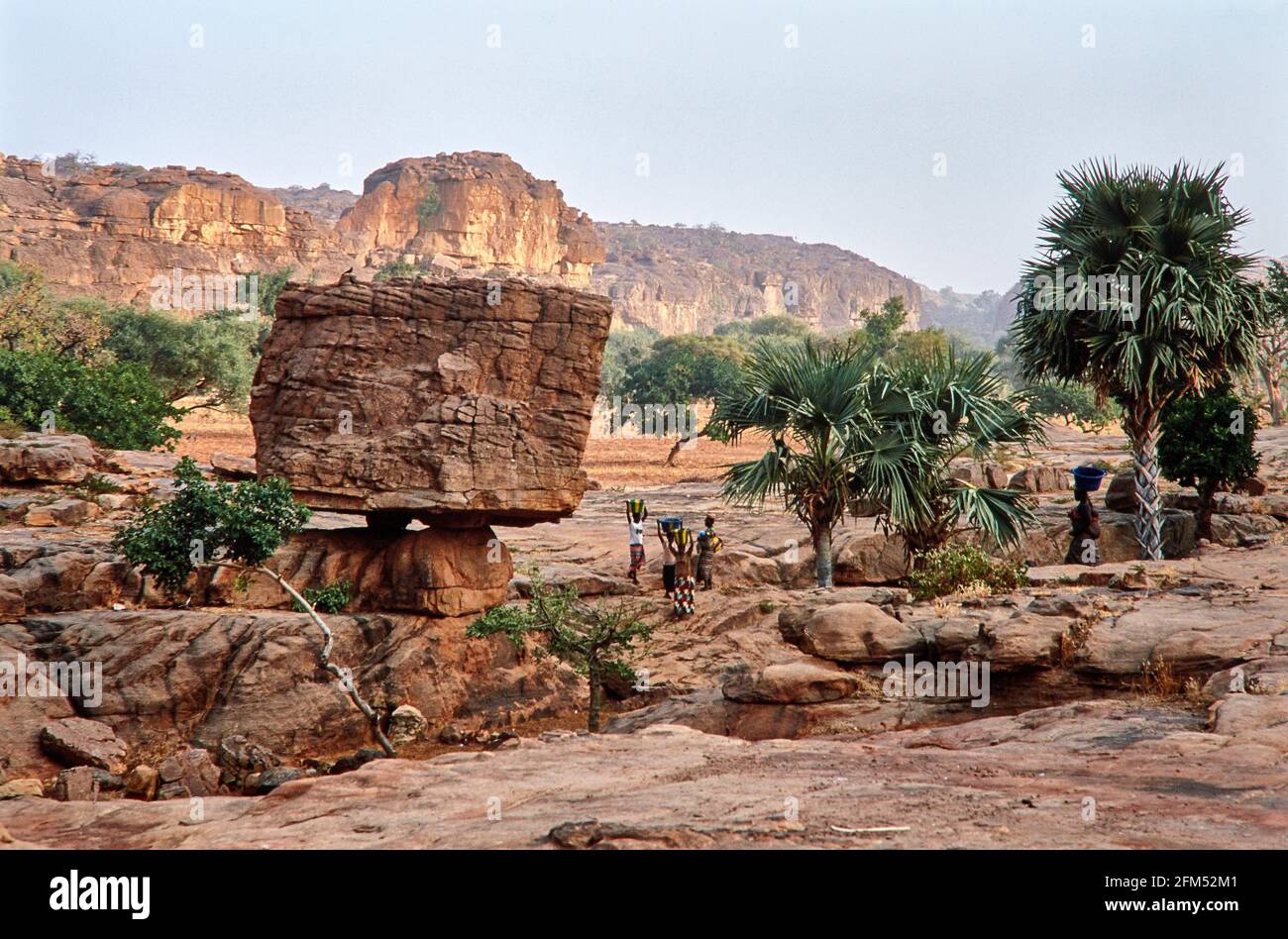 Strange rock formation in front of the Falaise de Bandiagara. In between Dogon women carrying baskets on their heads.  08.11.2003 - Christoiph Keller Stock Photo