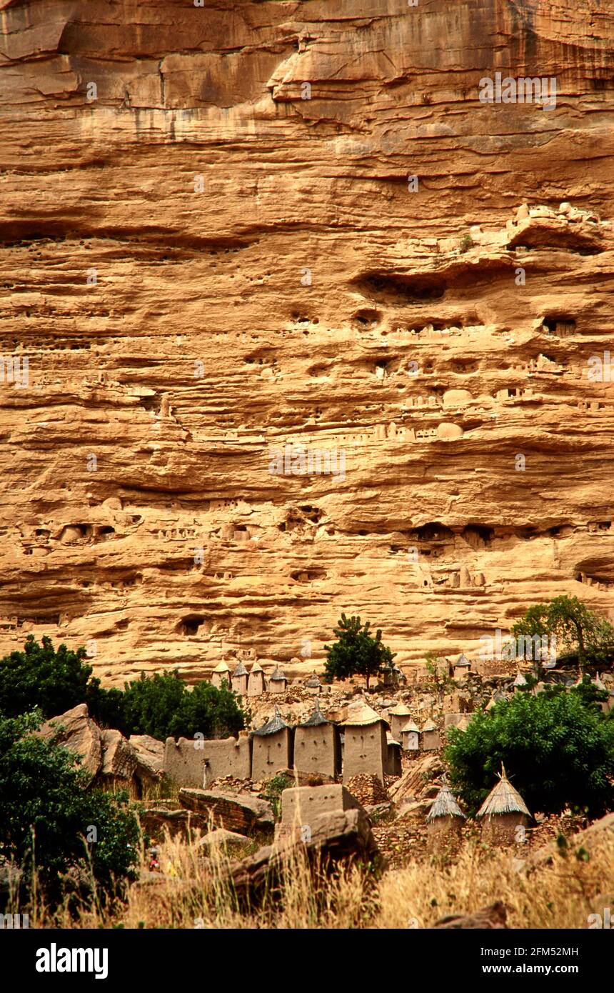 A Dogon village at the foot of the  Falaise de Bandiagara. The pointed thatched roofs belong to the village pantries. In the rock face you can see the Stock Photo