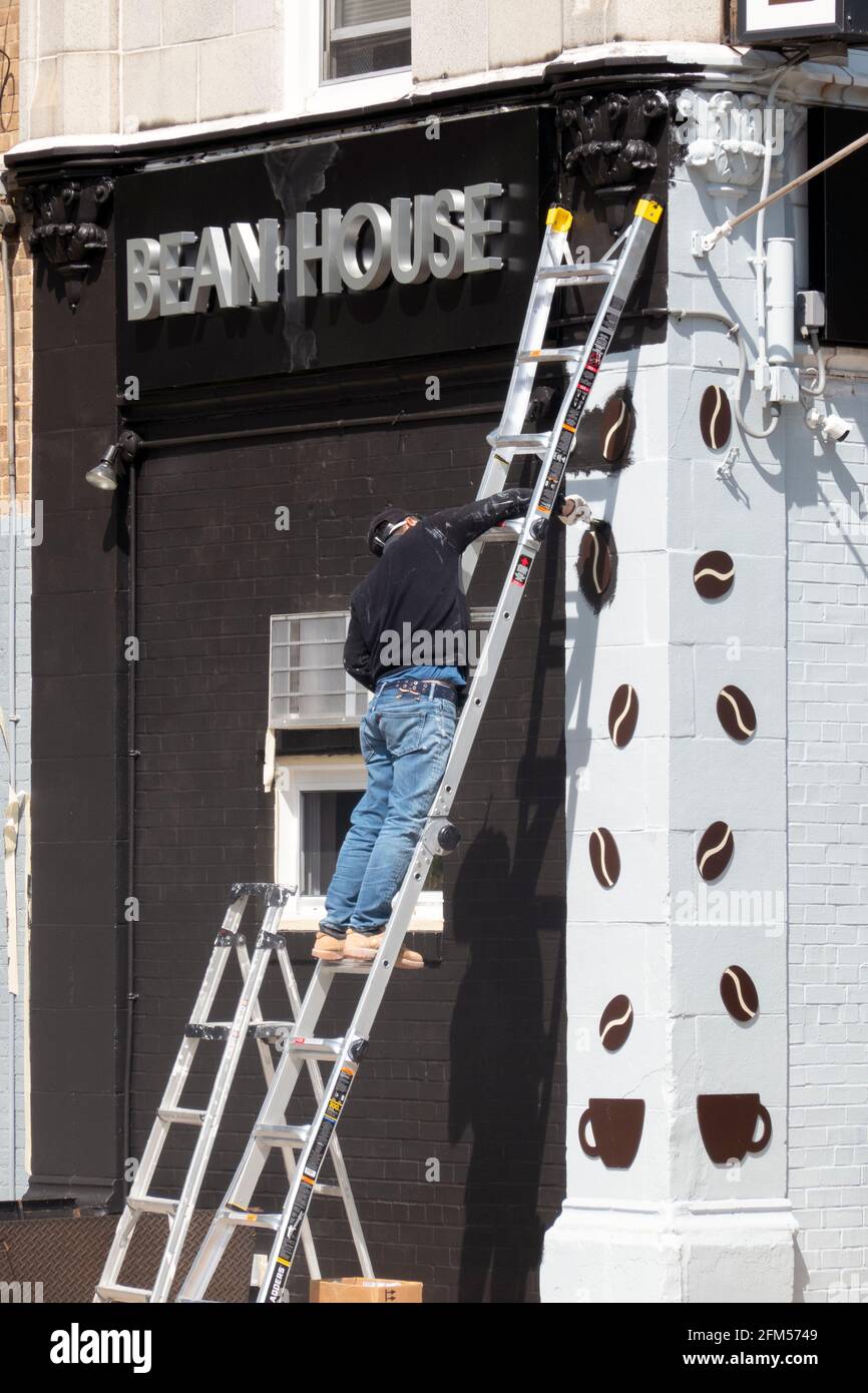 A painter paints a sign for a new business opening up on 29th Avenue in Flushing, Queens, New York City. Stock Photo