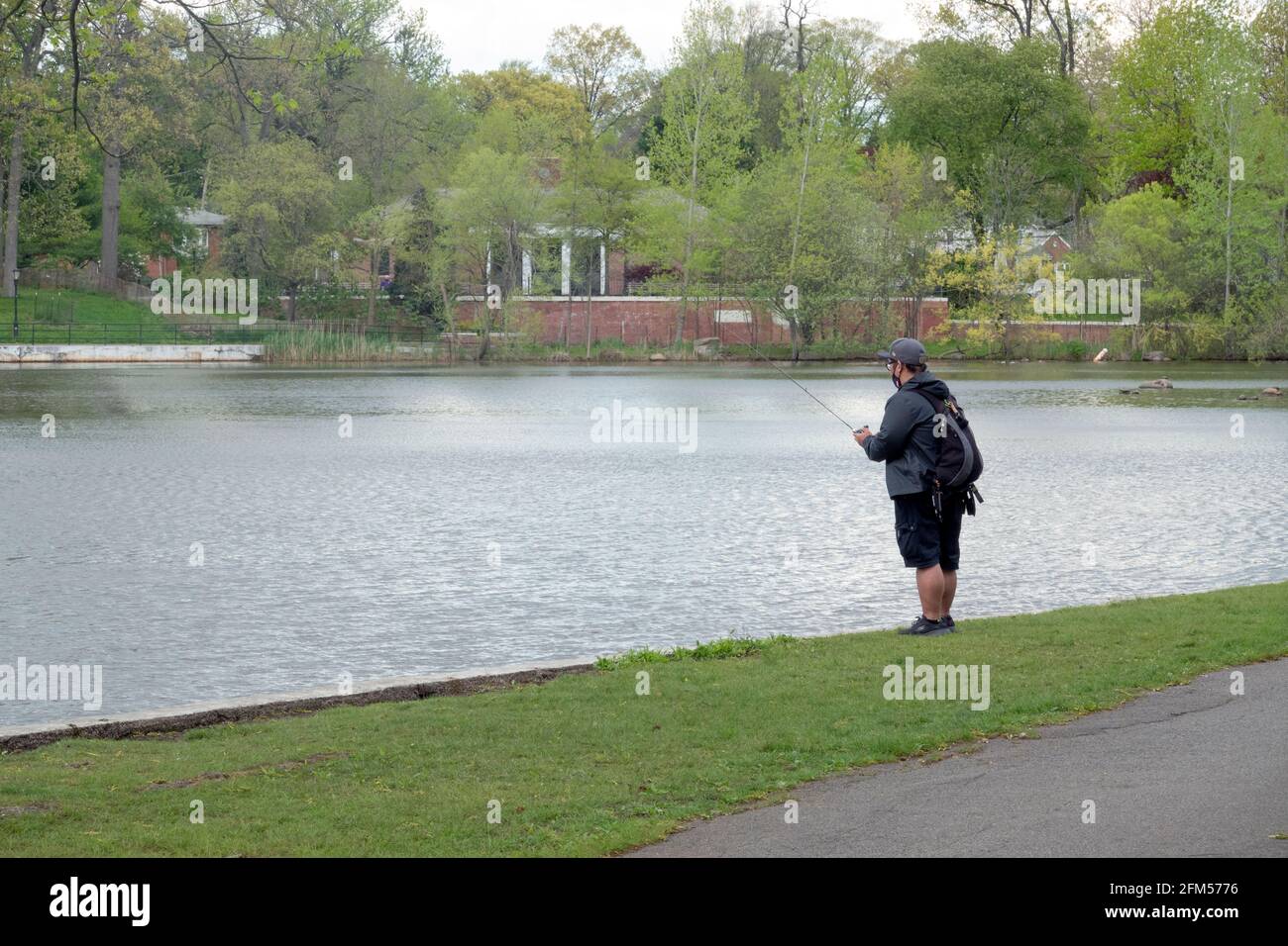 An Asian American man wearing a backpack fishes in the lake at Kissena Park in Flushing, Queens, New York City. Stock Photo