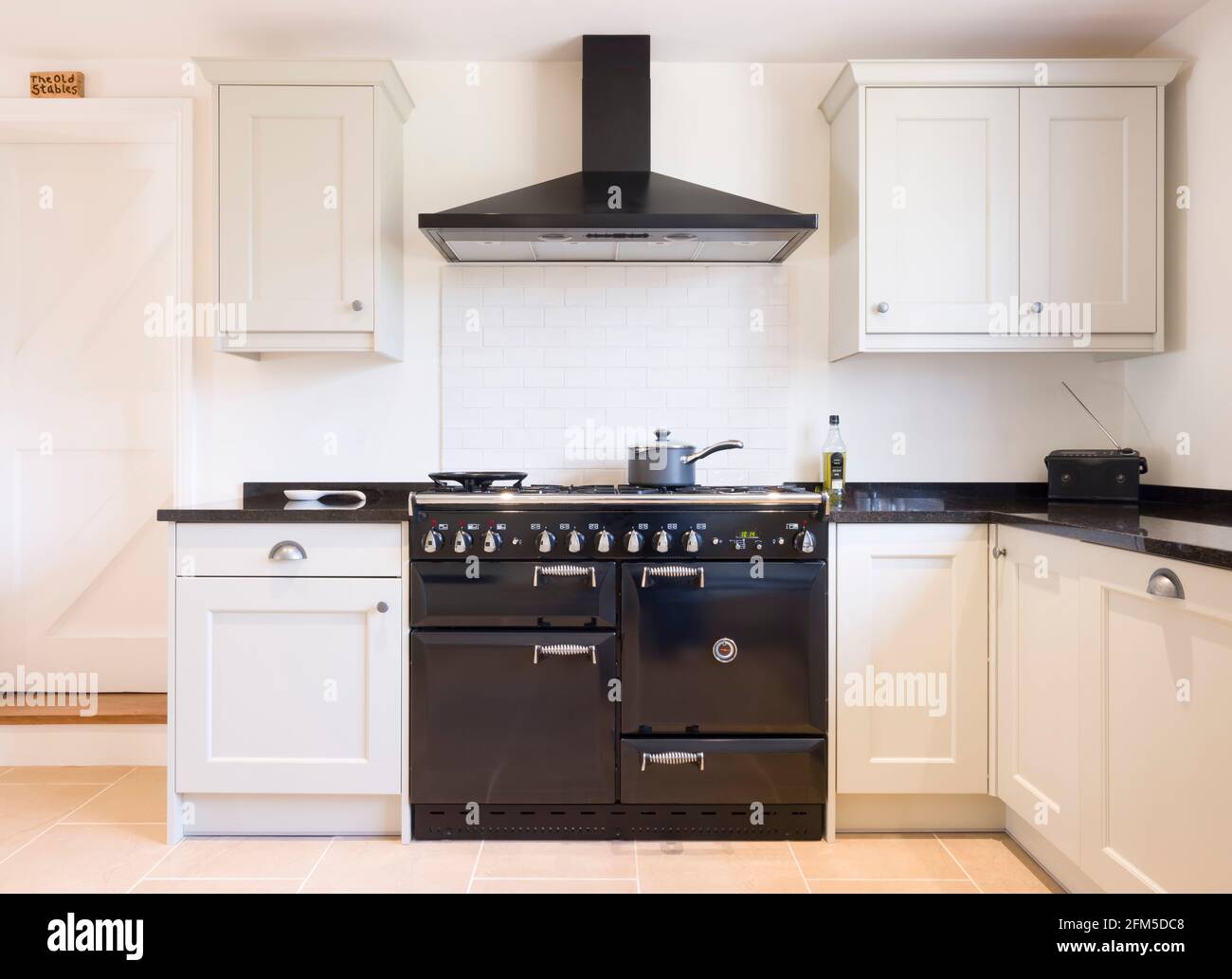 Modern modular kitchen interior in black and off white, with range cooker and chimney extractor hood. UK painted wood farmhouse kitchen design. Stock Photo