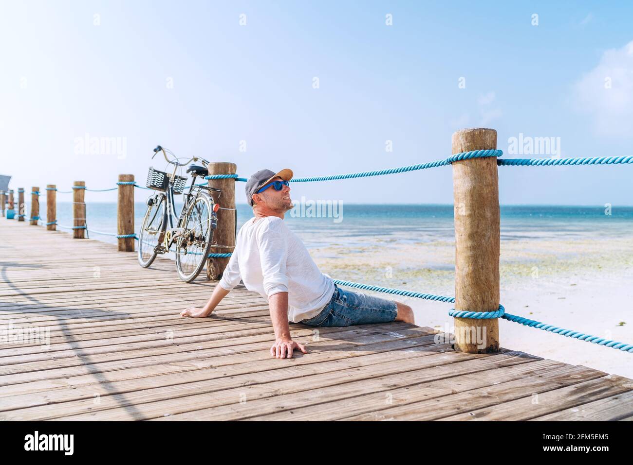 Portrait of relaxing man dressed in light summer clothes and sunglasses sitting and enjoying time and beach view on wooden pier.Careless vacation in t Stock Photo Alamy