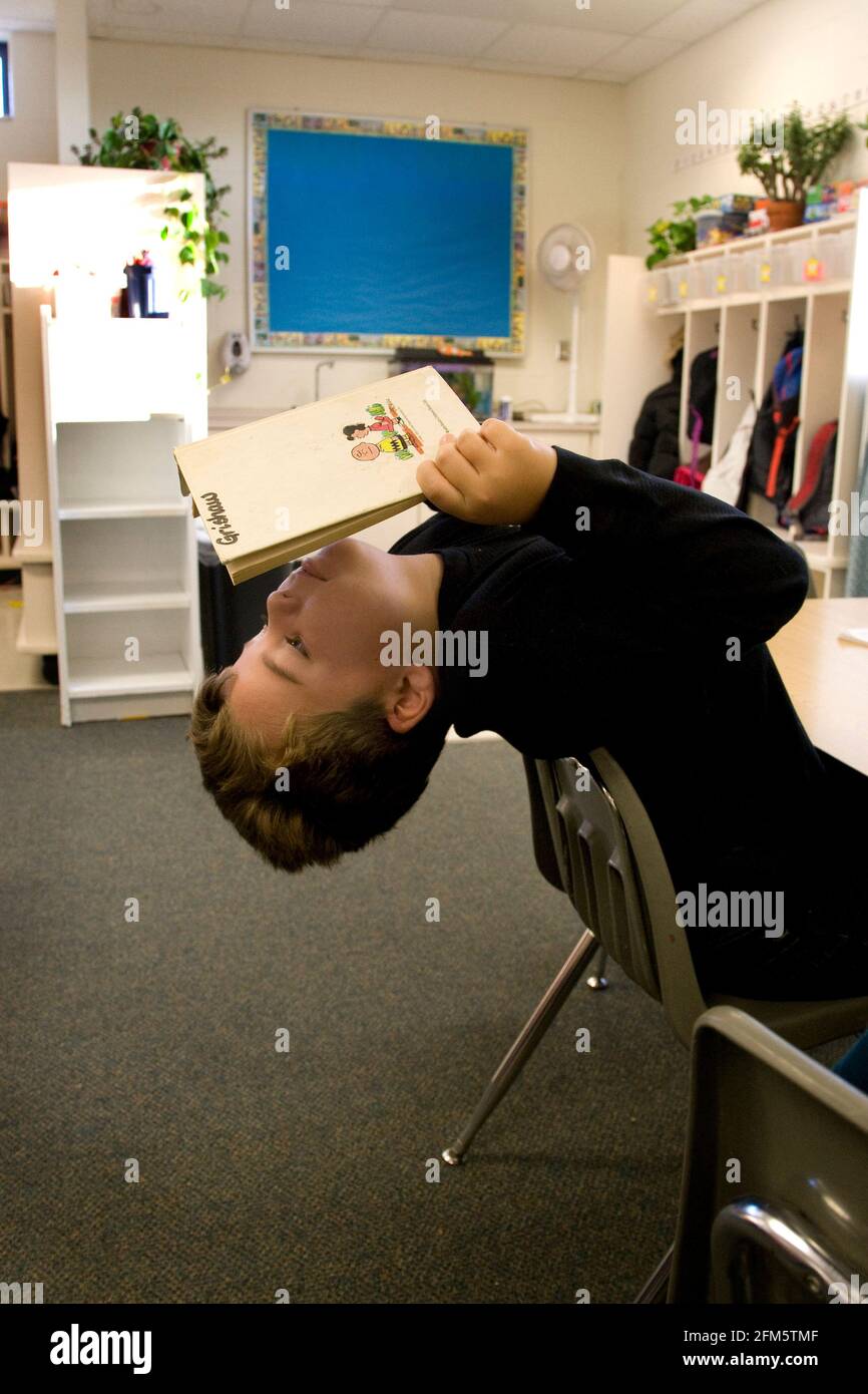 Elementary school boy leans way back in his classroom chair as her