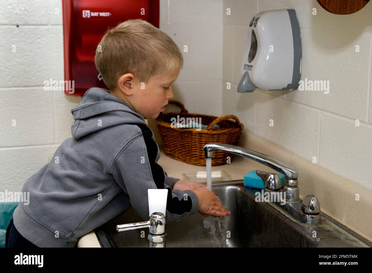 Elementary school boy washing his hands at a classroom sink in Suttons