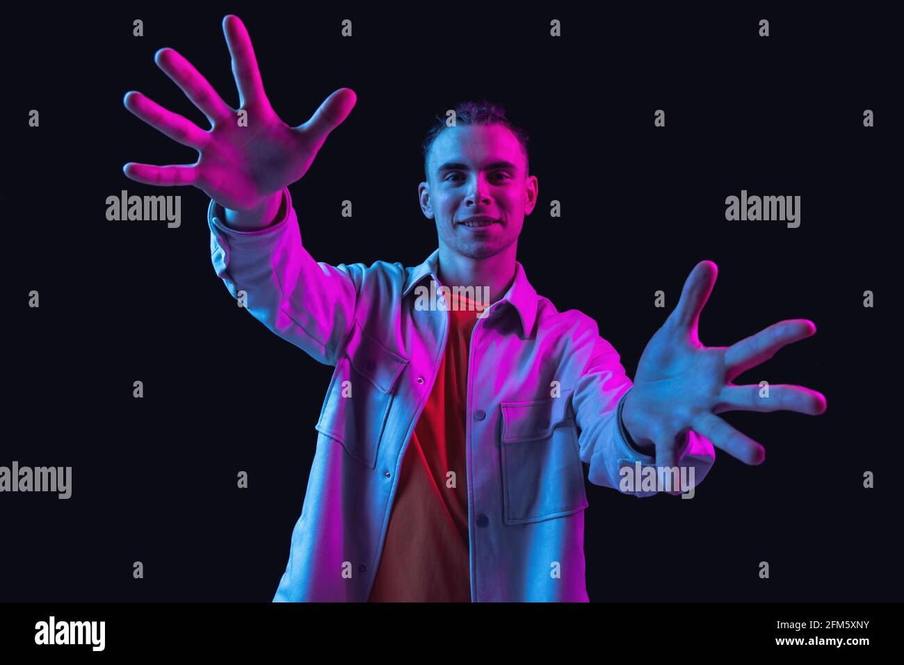 Caucasian young man's portrait on dark studio background in neon ...