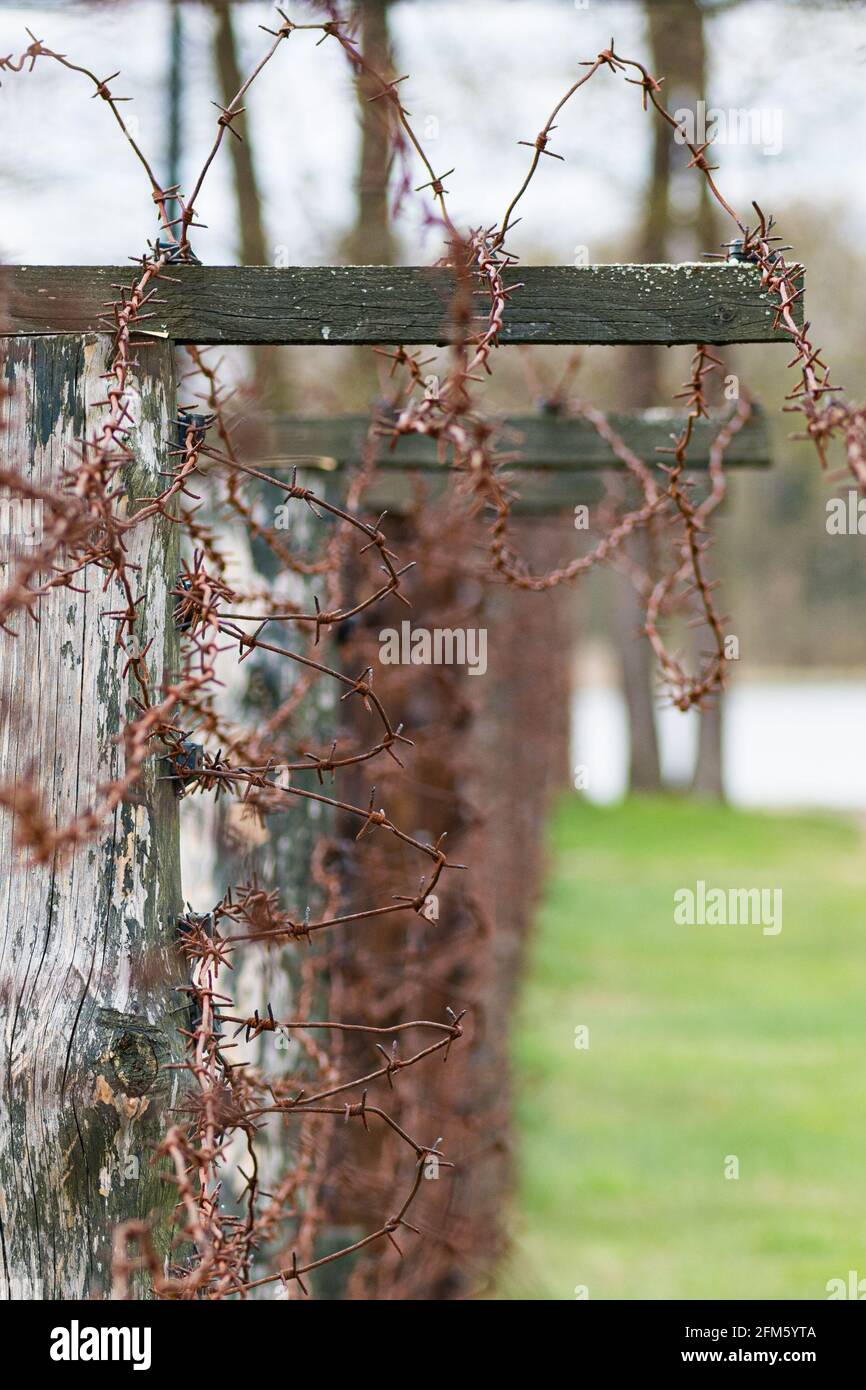 Close-up of a rusty barbed wire fence surrounding a detention, concentration and extermination camp, focus in the background, color, vertical Stock Photo