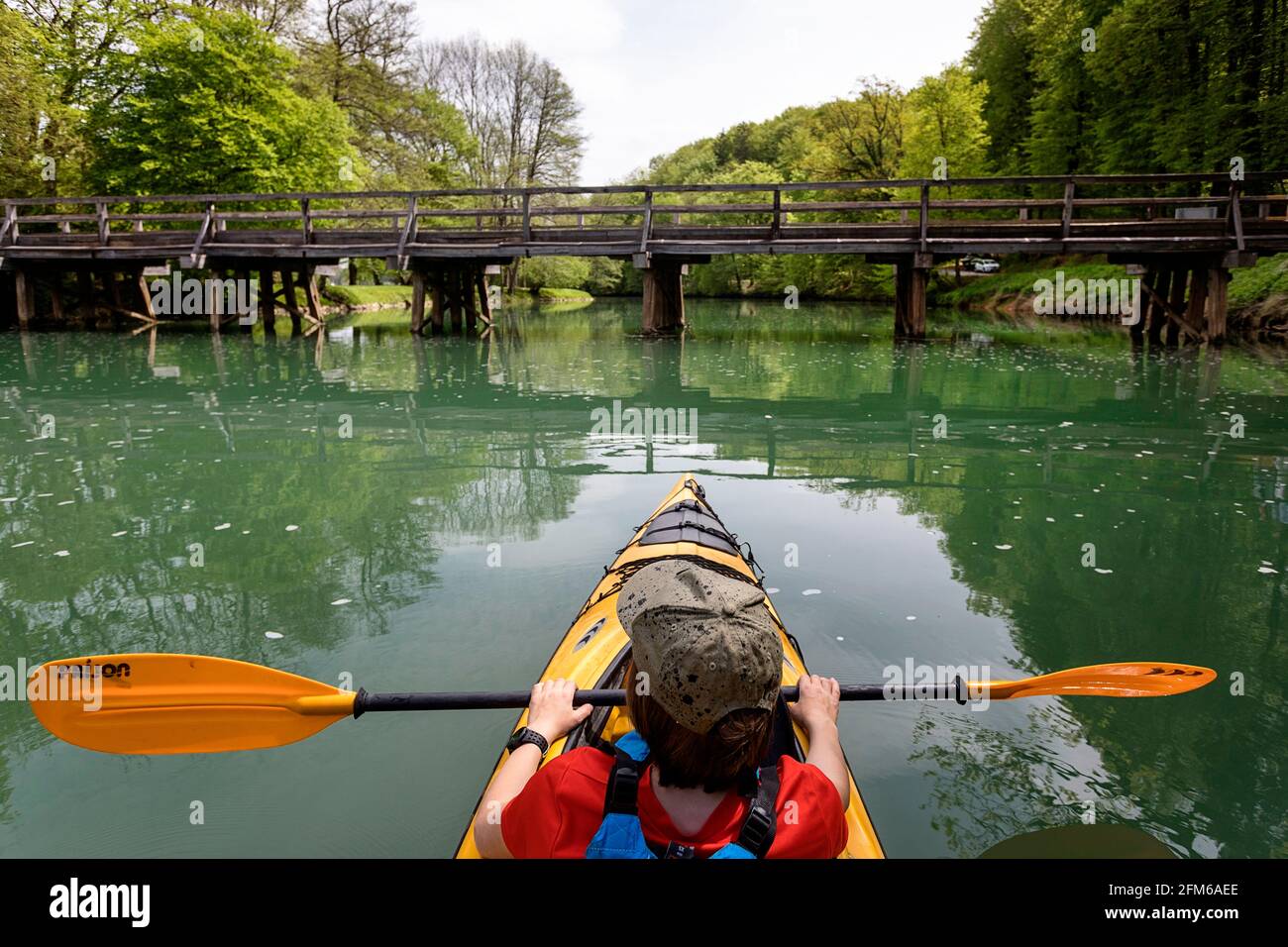 Young boy in yellow kayak on Krka river in front of the bridge, Otočec, Slovenia Stock Photo