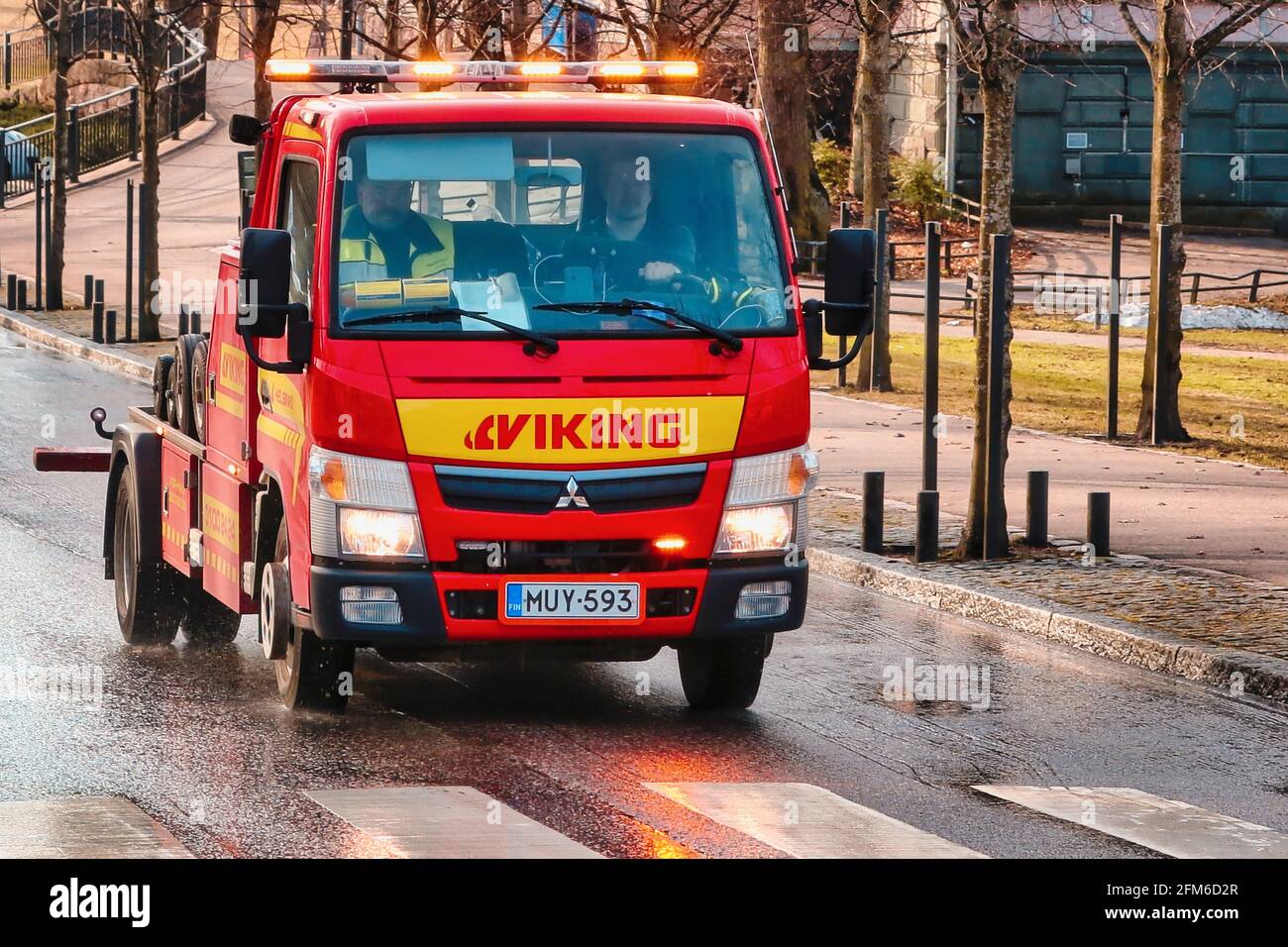 Red Mitsubishi wheel-lift tow truck of Viking Assistance Oy driving on the street in the morning, lights flashing. Helsinki, Finland. April 15, 2021. Stock Photo