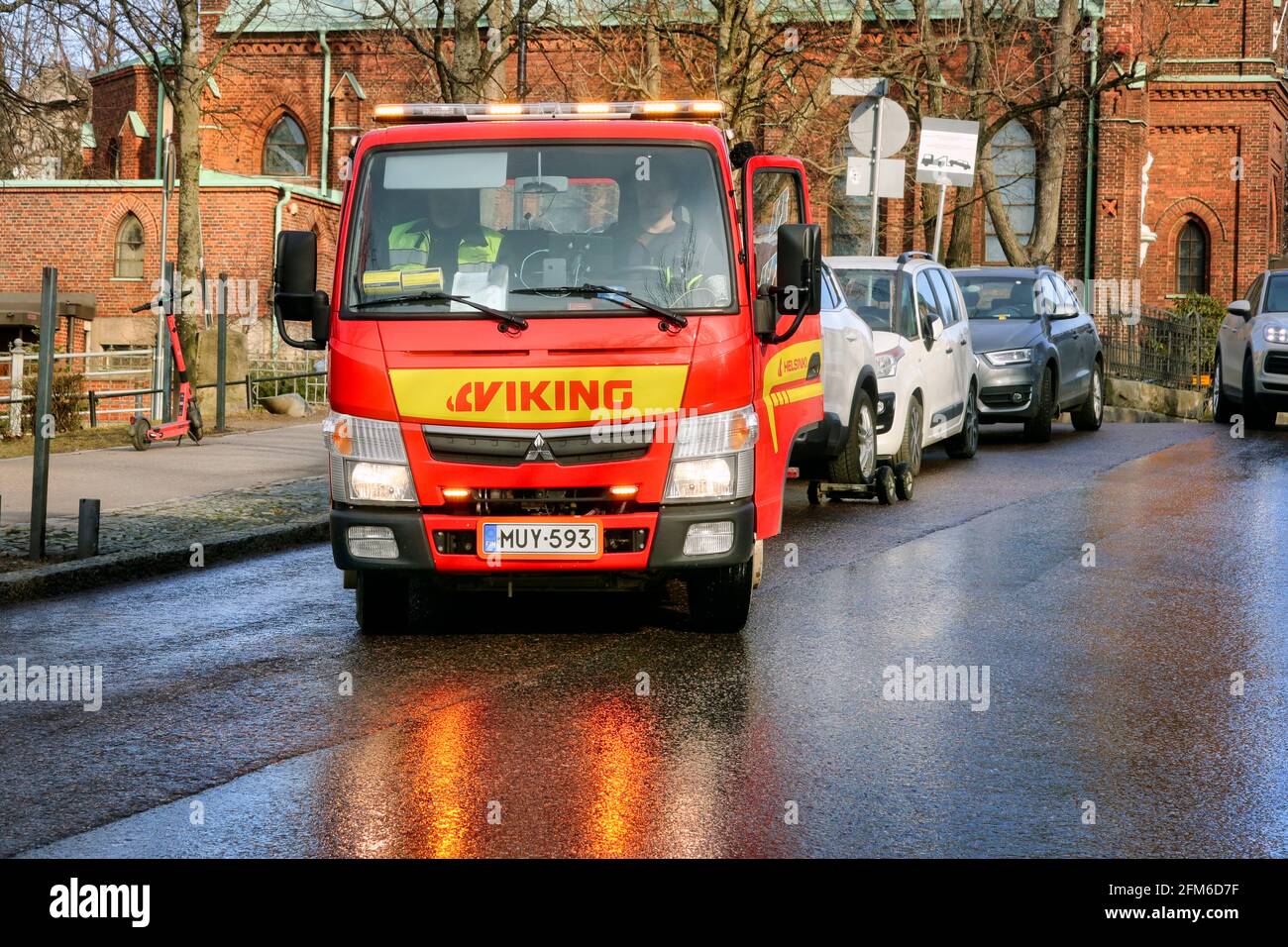 Red Mitsubishi wheel-lift tow truck of Viking Assistance Oy at work in city, lights reflecting on street. Helsinki, Finland. April 15, 2021. Stock Photo