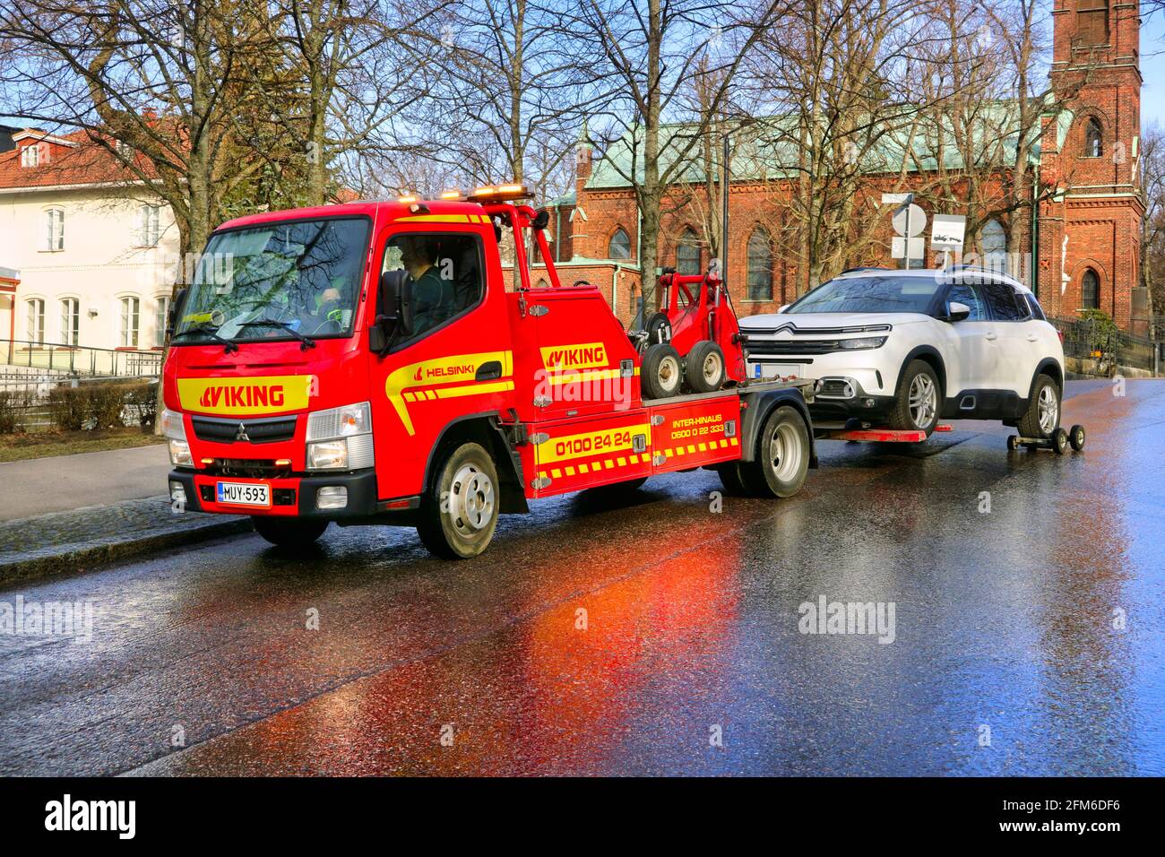 Red Mitsubishi wheel-lift tow truck of Viking Assistance Oy towing a car in city. Helsinki, Finland. April 15, 2021. Stock Photo