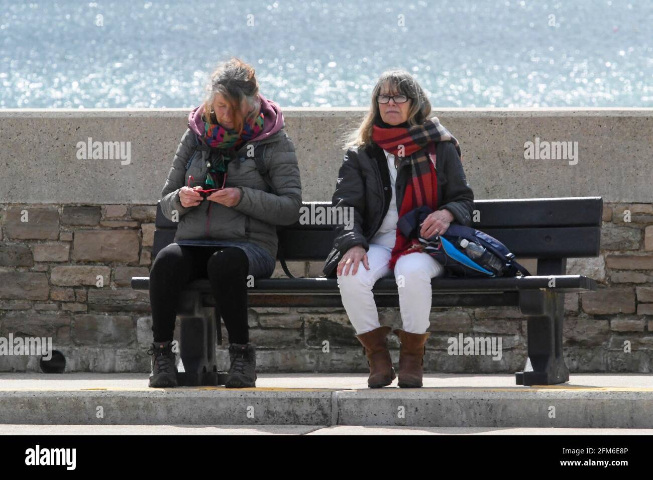 West Bay, Dorset, UK.  6th May 2021.  UK Weather.  Two women sitting on a bench enjoying the sunshine at the seaside resort of West Bay in Dorset on an afternoon of warm sunny spells.  Picture Credit: Graham Hunt/Alamy Live News Stock Photo