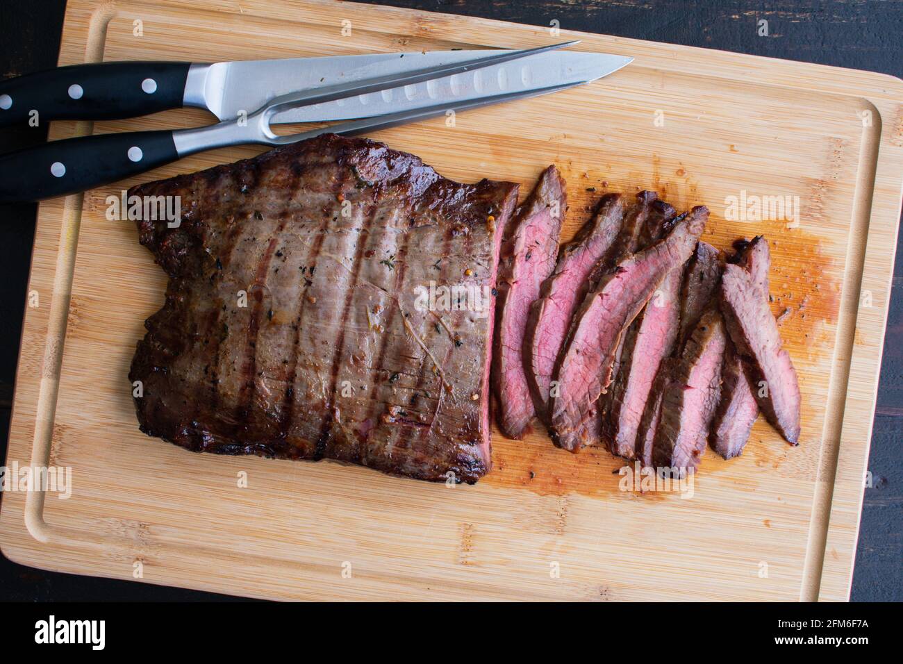 Bourbon Marinated Grilled Flank Steak: Sliced medium-rare flank steak on a bamboo carving board Stock Photo
