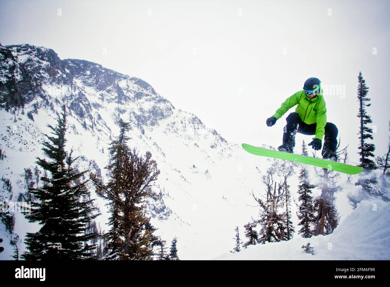 Snowboarder wearing green in mid-air after launching off snow jump. Stock Photo