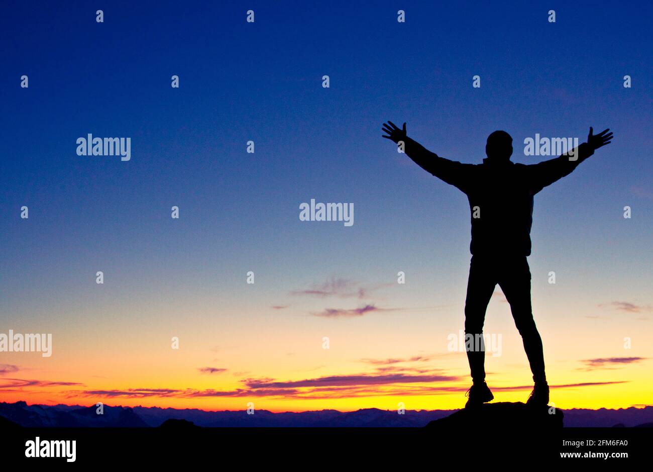 Silhouetted hiker standing on mountain summit with arms raised Stock Photo