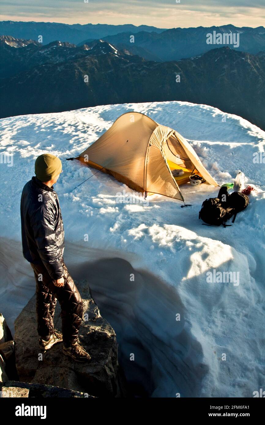 Man standing on mountain summit, looking out at tent and scenic view Stock Photo