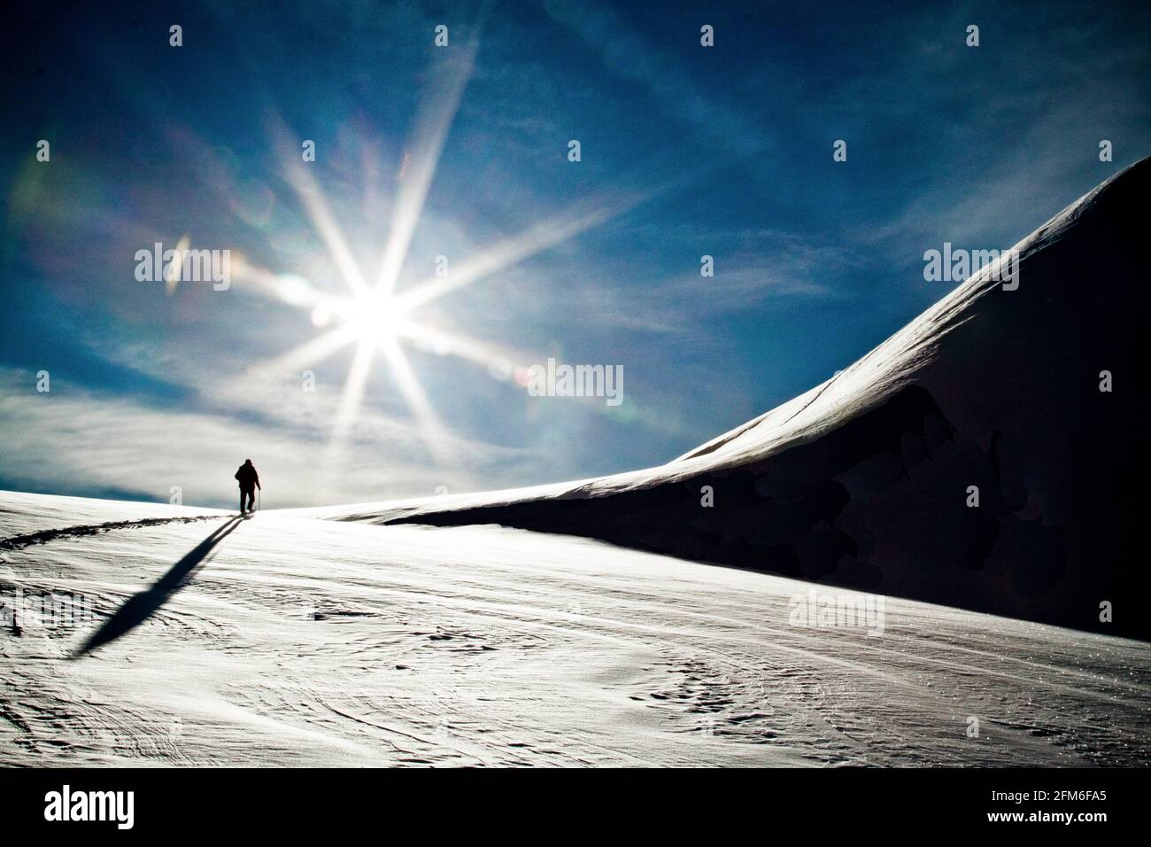 Rear view of silhouetted person ski touring towards snowy mountain. Stock Photo