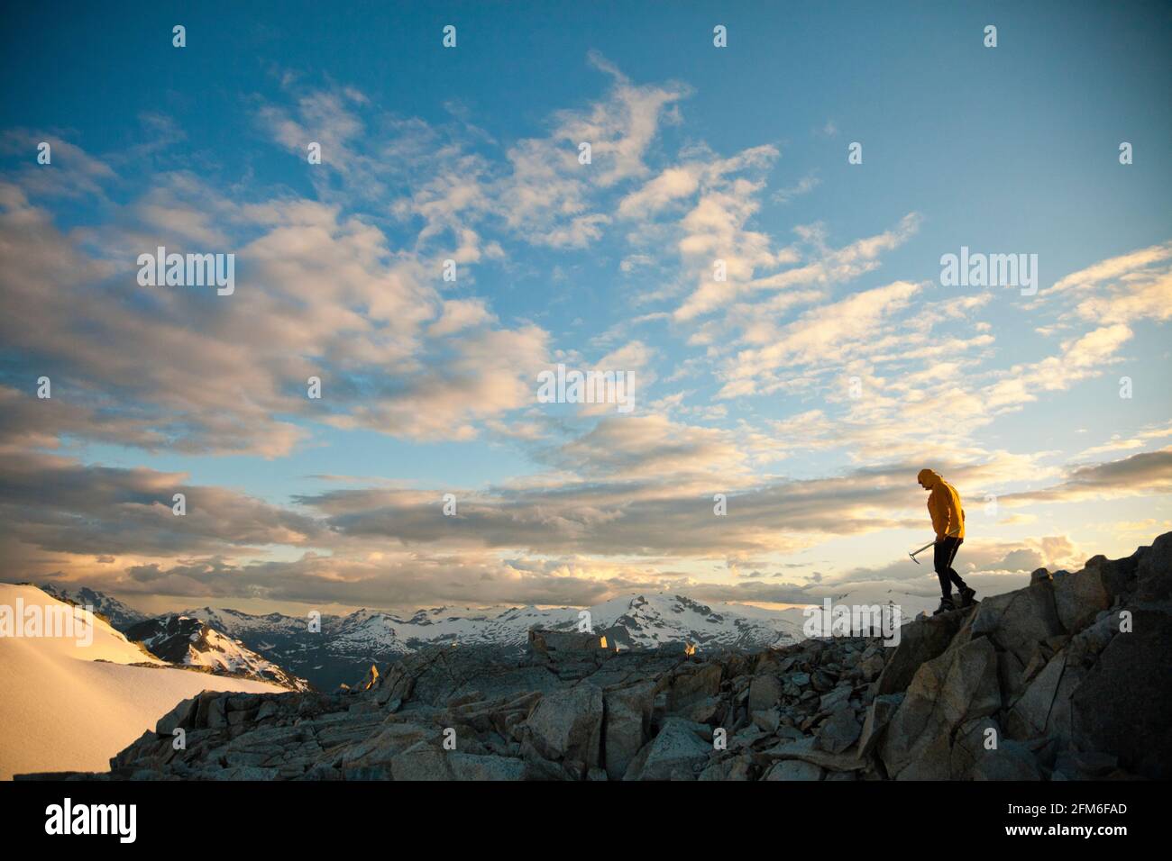 Mountaineer holding ice axe navigates a rocky mountain ridge. Stock Photo