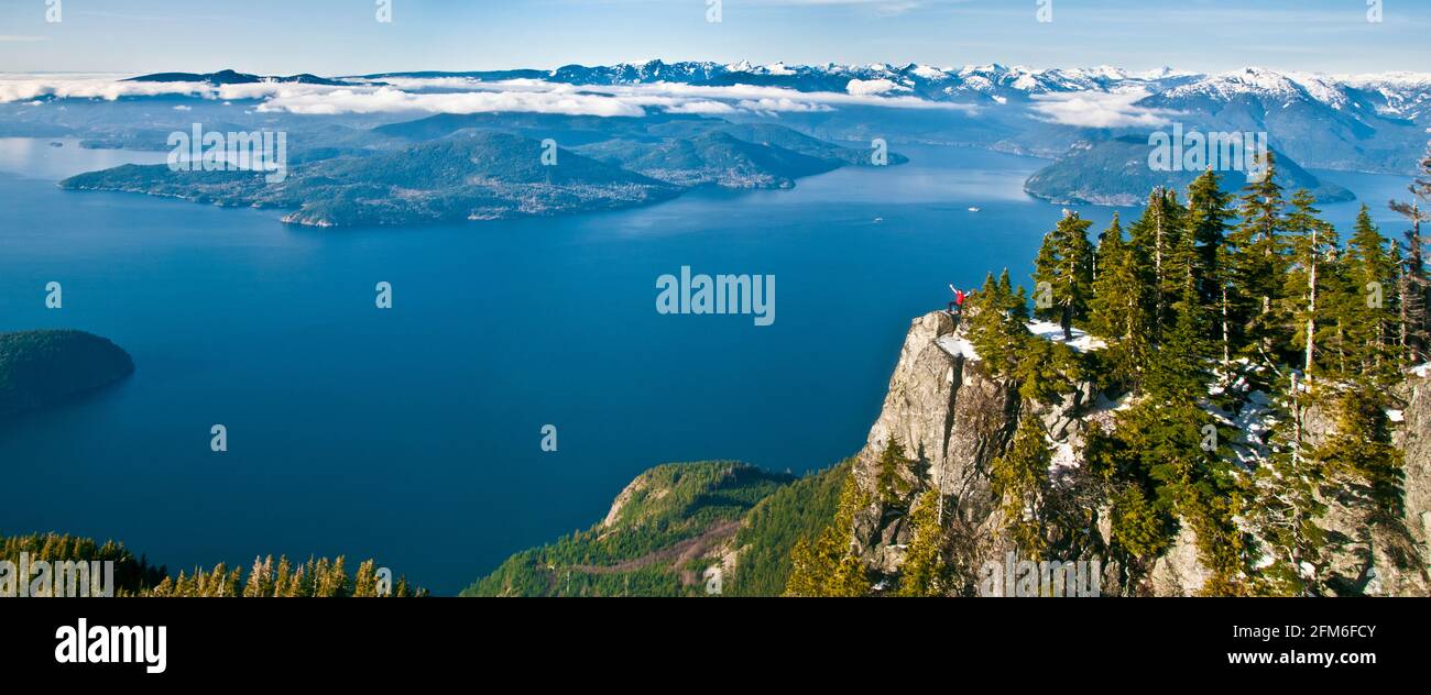 Panoramic view of hiker standing on mountain summit, Vancouver B.C. Stock Photo