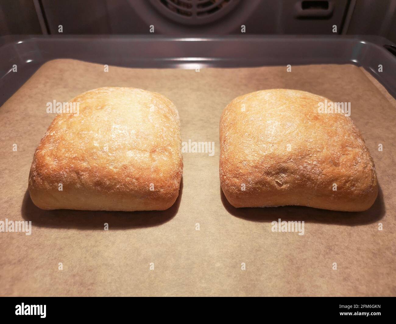 Two loaves of bread are baked on baking trays on baking paper in the oven Stock Photo