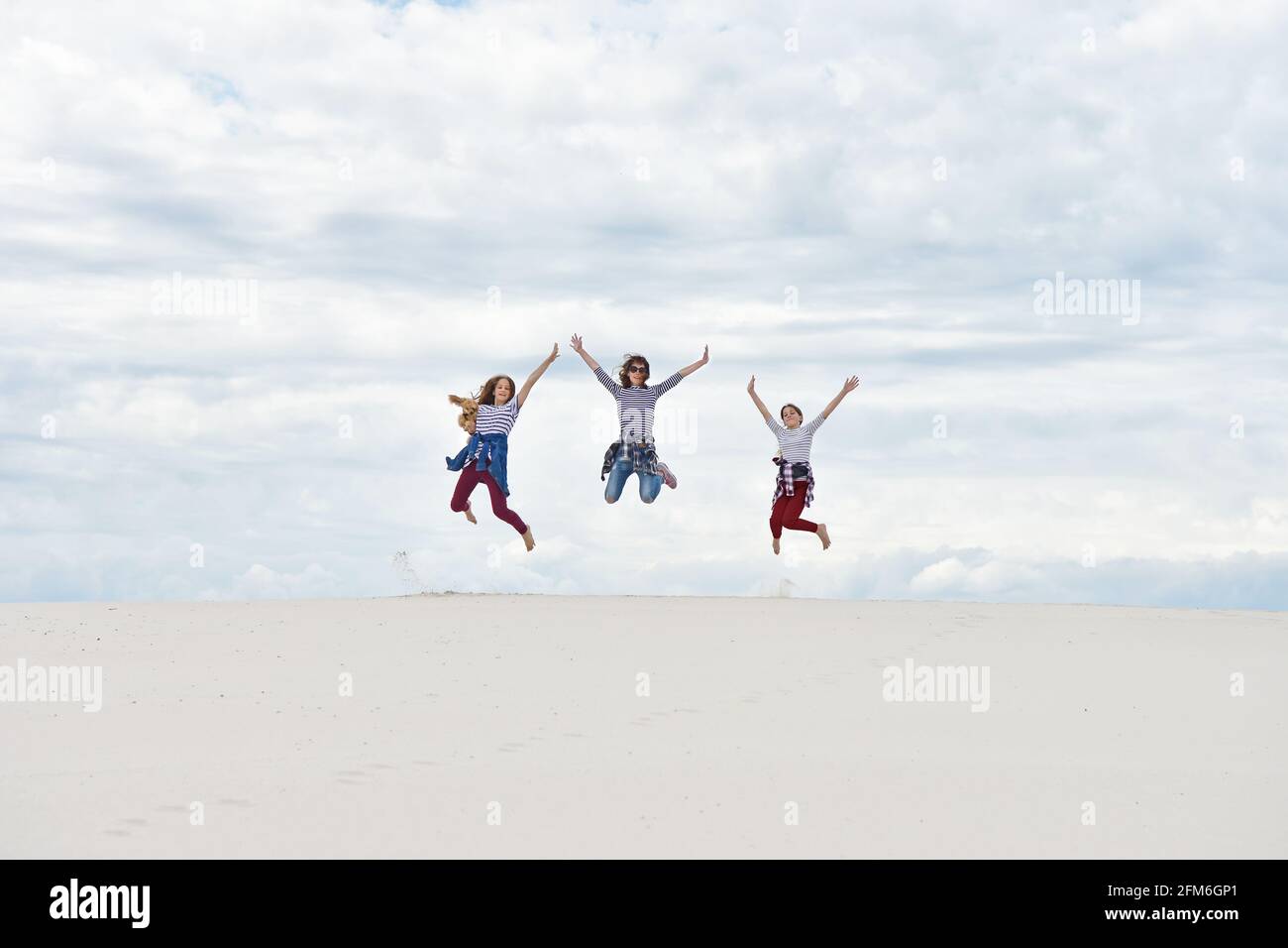 Girls with mom are jumping against the background of the sky and sand Stock Photo