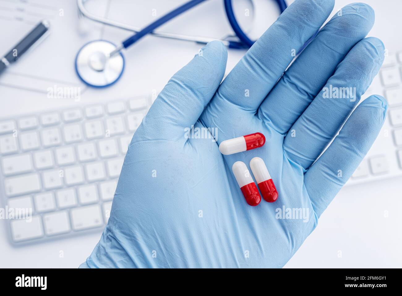 Human hand in protective glove holding pills and doctor desk at background. Medicine or Medicament concept Stock Photo
