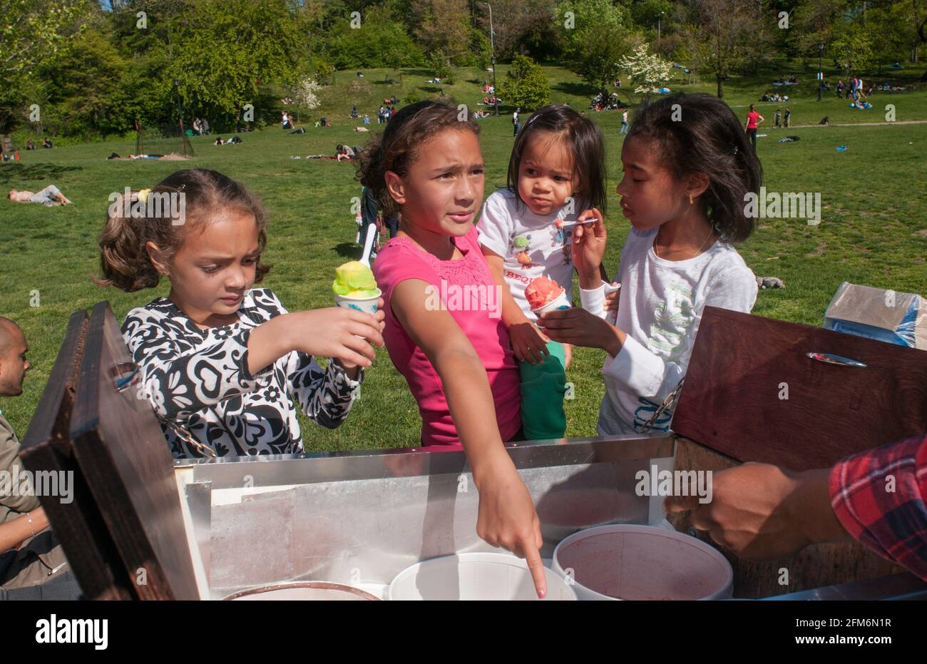 Four bi-racial girls place an order with an ice cream vendor in Prospect Park in Brooklyn, NY. They are near the Grand Army entrance. Stock Photo