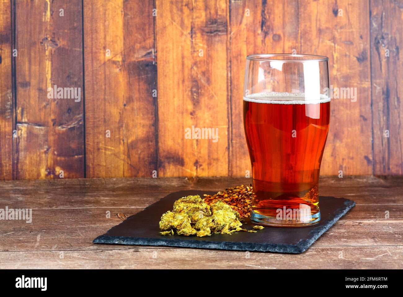 Pint glass filled with beer at the side of a slate filled with hops and brewers barley malt Stock Photo