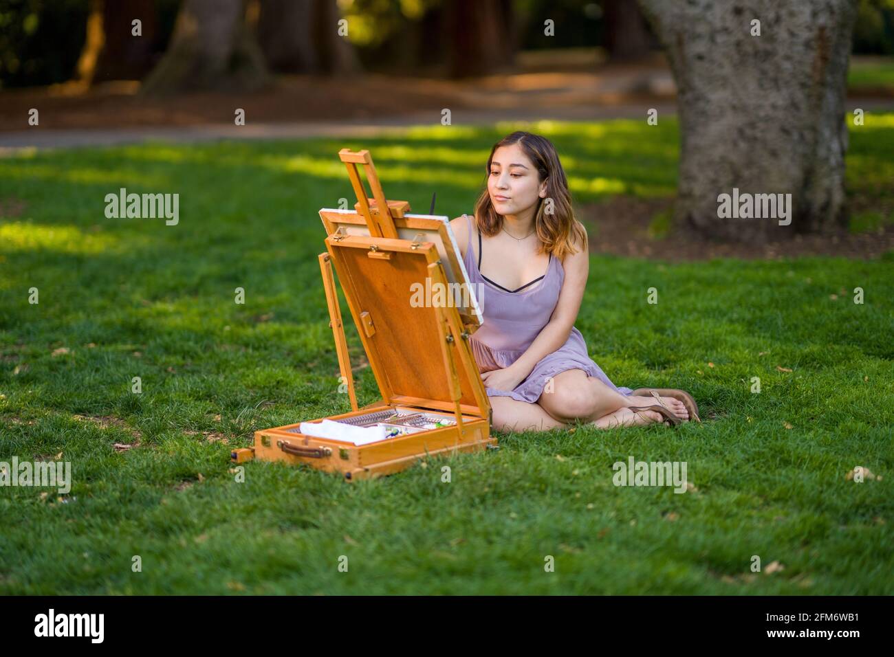 Petite Young Asian Woman Student Painting in the Park Using a Cabinet Easel Stock Photo