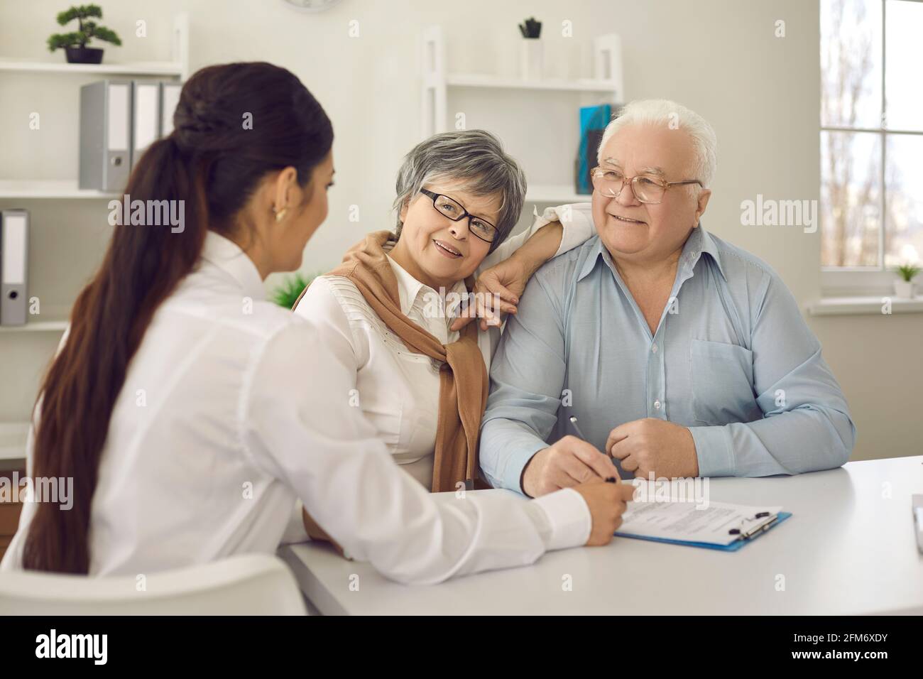 Happy senior couple talking to family practitioner sitting at table at doctor's office Stock Photo