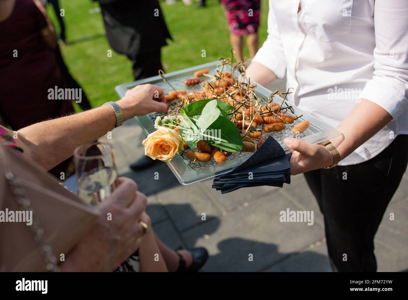 A guest takes a canape from a tray served by a waitress at an outdoor party  or wedding Stock Photo - Alamy