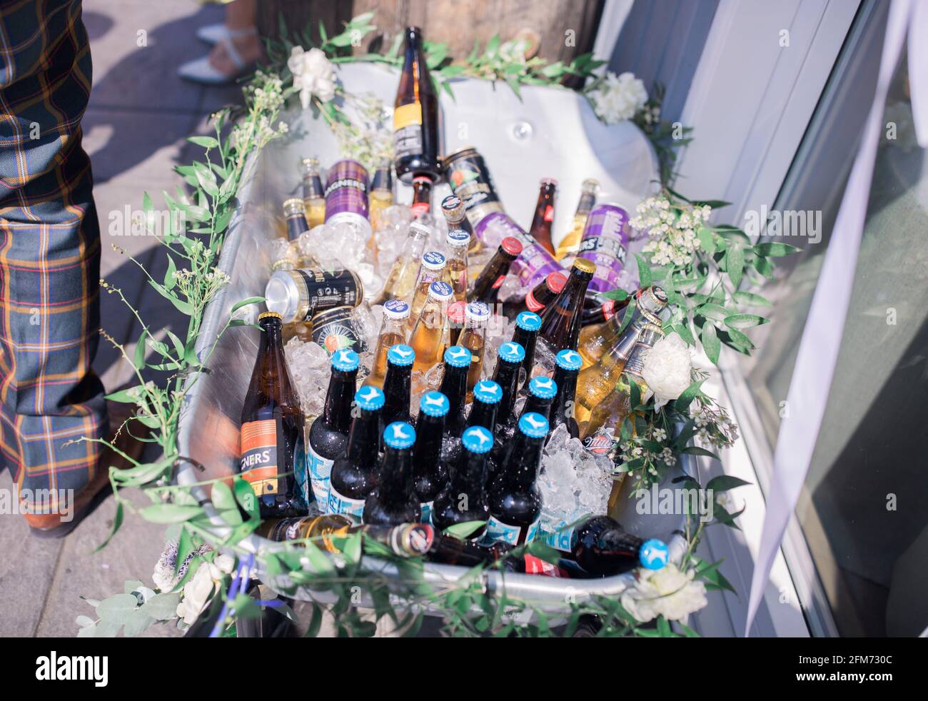 A box of beer and cider in ice outside at a party beside a man in tartan trousers Stock Photo
