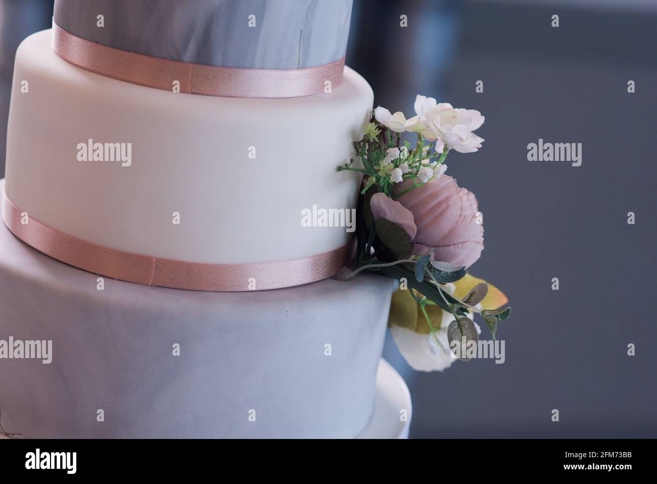 Close up of a grey and white three tier wedding cake with flowers and pink ribbon at an angle Stock Photo