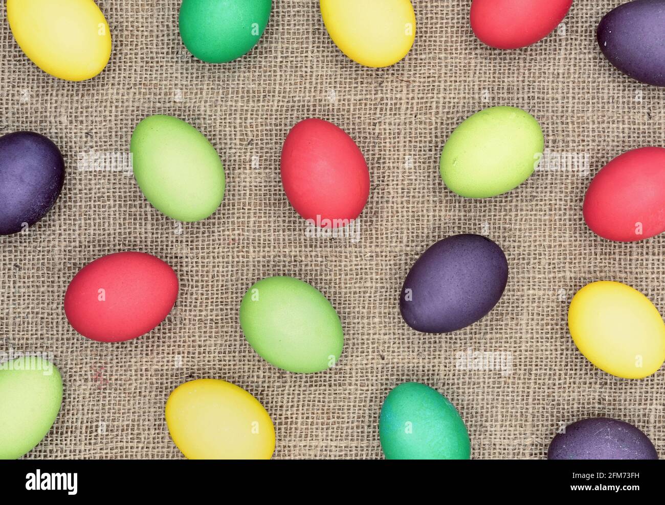 Background with multicolored easter eggs on a burlap. Stock Photo