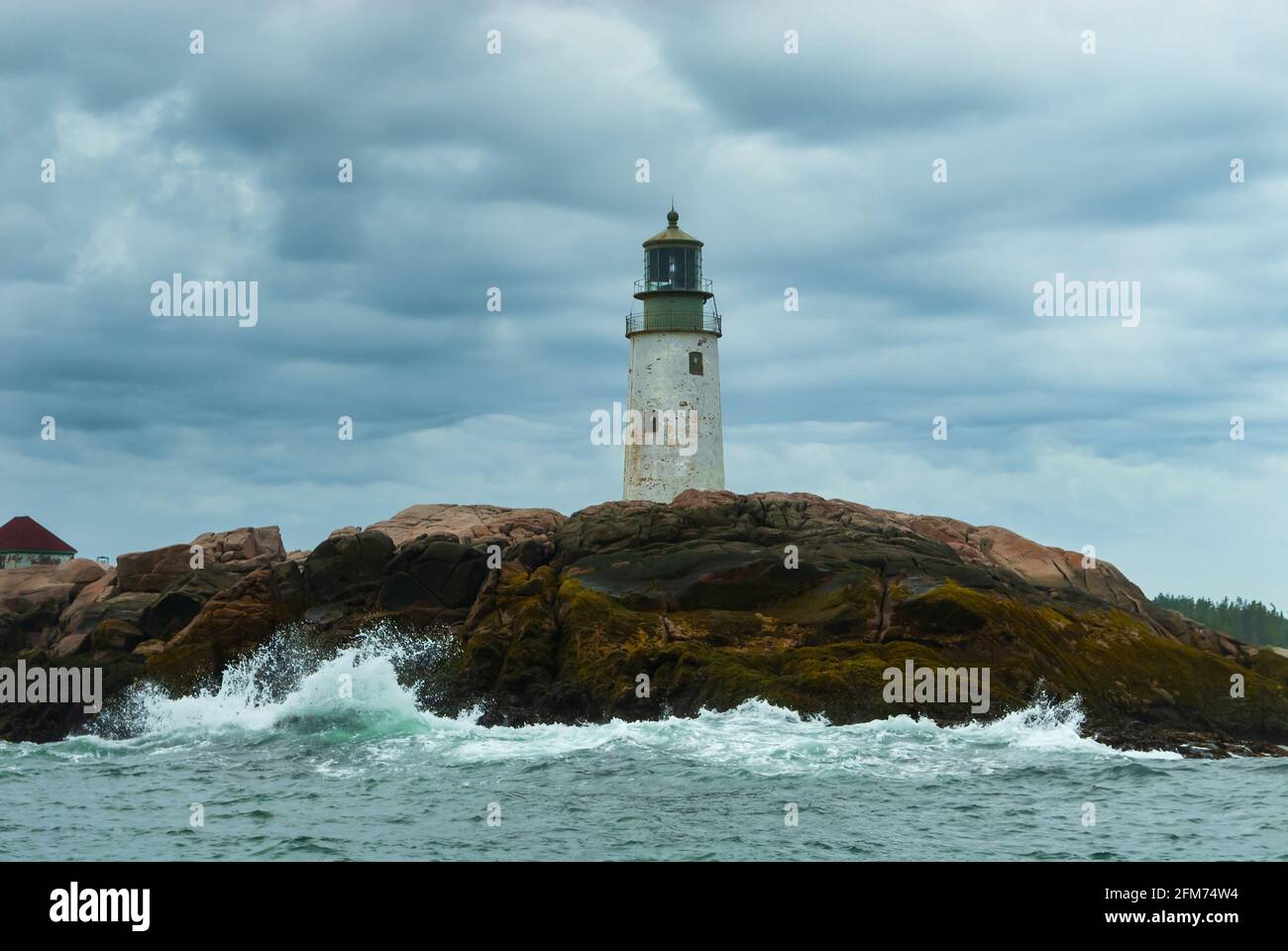 Waves break by old Moose Peak lighthouse tower on a rocky island, on a cloudy day as the sun breaks through storm clouds in Maine. Lighthouses of nort Stock Photo