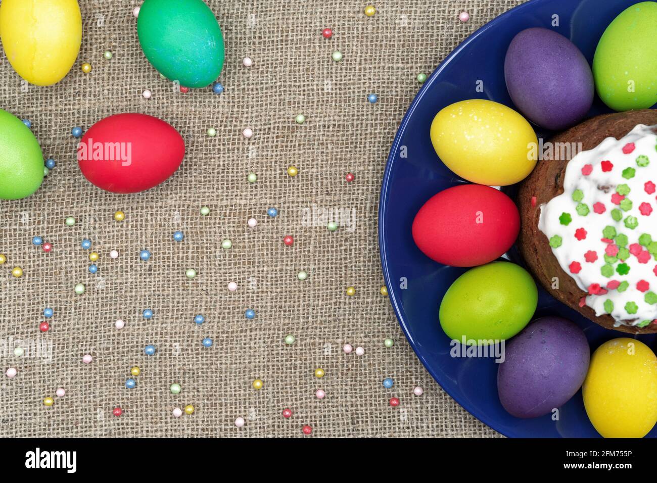 Round plate with multicolored Easter eggs and Easter cake on a burlap background. Stock Photo