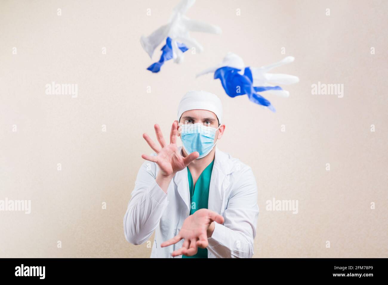 Young doctor portrait in white lab coat protective breathing mask throws down white and blue gloves on yellow background isolated. Stock Photo